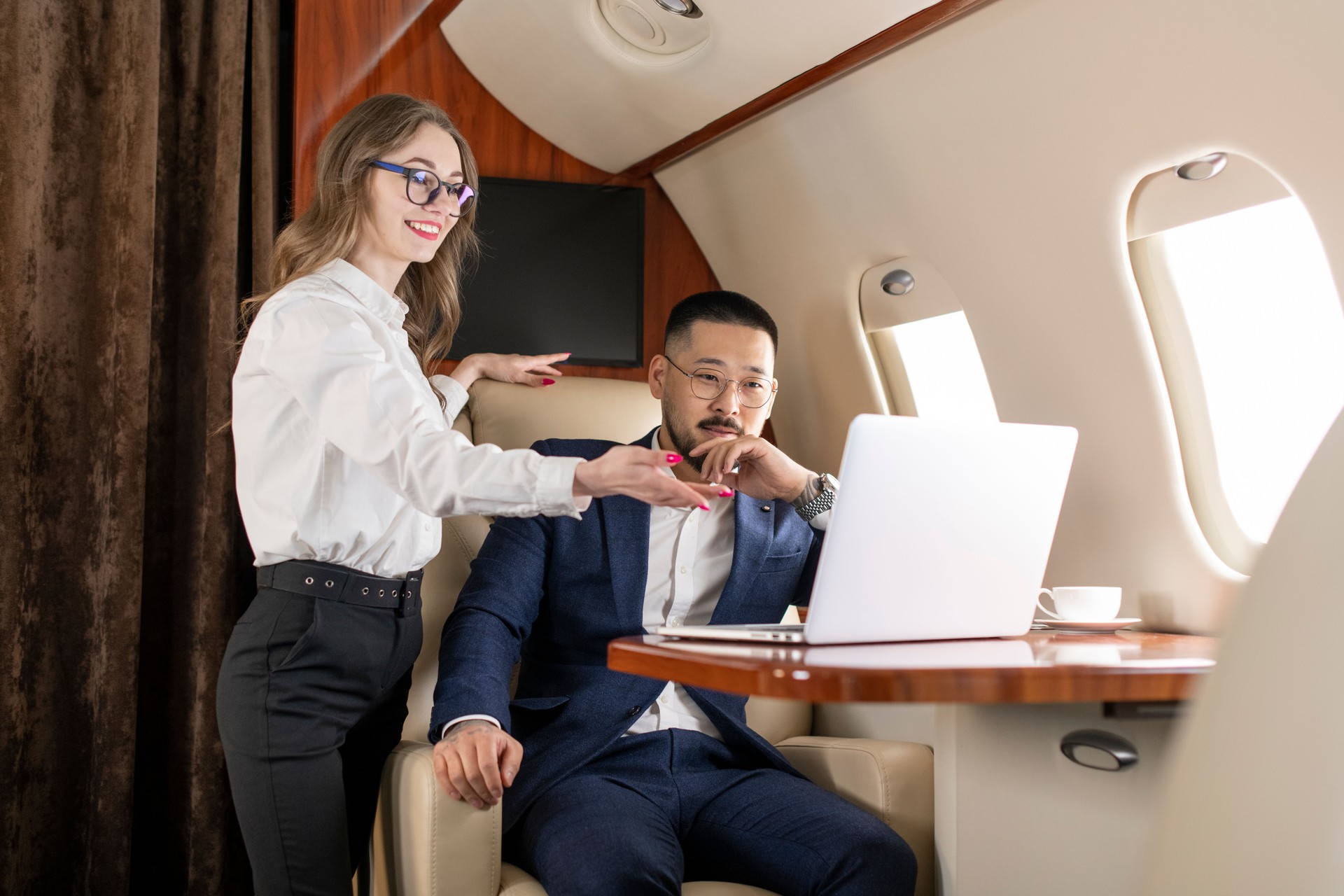 successful asian businessman in suit and glasses is flying in private luxury plane with female colleague